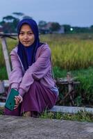 musulman femme est séance sur le bord de une riz champ avec sa mains ensemble. riz des champs Contexte avec copie espace. photo