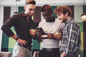 jeunes multiethniques prometteurs célébrant et buvant des toasts au whisky, regarder un gadget photo