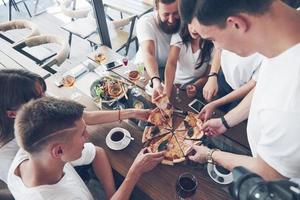 pizza savoureuse sur la table, avec un groupe de jeunes souriants se reposant dans le pub photo