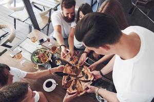 pizza savoureuse sur la table, avec un groupe de jeunes souriants se reposant dans le pub photo