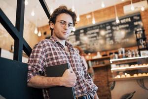 Jeune homme talentueux en chemise décontractée dessin croquis dans un ordinateur portable profitant du temps libre dans un café. Étudiant qualifié écrivant ses devoirs dans le bloc-notes assis dans le coworking photo