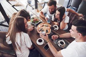 pizza savoureuse sur la table, avec un groupe de jeunes souriants se reposant dans le pub photo