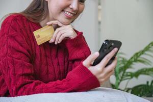 femme en portant crédit carte et en utilisant téléphone intelligent à maison, en ligne achats, en ligne bancaire, paiement, dépenses argent, commerce électronique à magasin, crédit carte concept photo