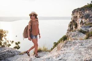 jeune fille avec sac à dos profitant du coucher de soleil au sommet de la montagne rocheuse. concept de vacances d'aventure de style de vie de voyage photo
