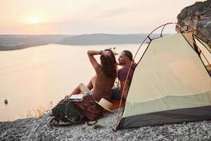 photo d'un couple heureux assis dans une tente avec vue sur le lac lors d'une randonnée. concept de vacances d'aventure de style de vie de voyage
