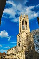 gothique église la tour contre une vibrant bleu ciel avec duveteux des nuages, mettant en valeur complexe architectural détails et une épanouissement arbre à le coin dans York, Nord Yorkshire, Angleterre. photo