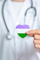 queer fierté journée et lgbt fierté mois concept. médecin main en portant violet, blanc et vert cœur forme avec stéthoscope pour lesbienne, gay, bisexuel, transgenres, genderqueer et pansexuel communauté photo