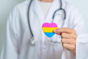 pansexuel fierté journée et lgbt fierté mois concept. médecin main en portant rose, Jaune et bleu cœur forme pour lesbienne, gay, bisexuel, transgenres, queer et pansexuel communauté photo