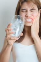 les dents sensible à du froid concept. femme tenir la glace l'eau verre et ayant mal aux dents et douleur après manger. dent pourriture ou gencive maladie, broyage les dents et stress, exposé nerf racines, fissure et fuyant les gencives photo