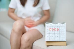 menstruation période cycle de mensuel et maux d'estomac concepts. femme ayant abdomen douleur avec calendrier, maladies femelle souffrir de prémenstruel mal et corps santé problème sur canapé à Accueil photo