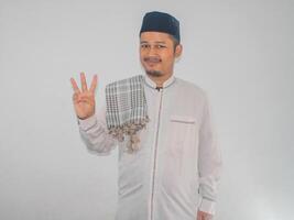 musulman asiatique homme souriant à le caméra et montrant Trois les doigts signe photo