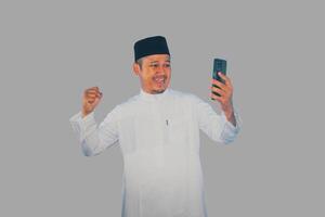 musulman asiatique homme serré poing montrant excitation tandis que à la recherche à le sien mobile téléphone photo