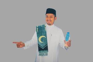 musulman homme souriant tandis que en portant une bouteille de en buvant l'eau et montrer du doigt à le droite côté photo