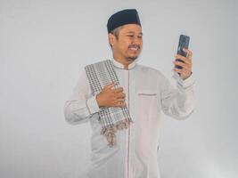 asiatique musulman homme souriant content lorsque dans appel en utilisant mobile téléphone photo