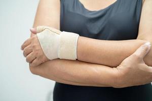 une femme asiatique d'âge moyen utilise un bandage élastique pour traiter le syndrome de de quervain à la main et au doigt au bureau. photo