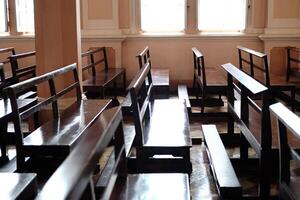 ancien longue en bois chaises pour séance et prier pour bénédictions dans Christian des églises. Lignes de église bancs dans lumière du soleil photo