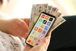 Kyiv, Ukraine - avril 1, 2024 asiatique applications icône sur téléphone intelligent écran et argent dans femelle main photo