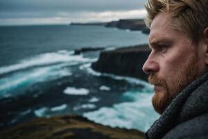 une homme avec une barbe et rouge cheveux regards en dehors plus de le océan photo