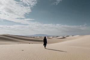 une femme dans une noir robe en marchant dans le désert photo
