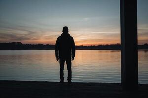 une homme permanent sur une Dock à le coucher du soleil photo