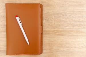 une fermé carnet avec une cuir couverture et une stylo sur le en bois table photo