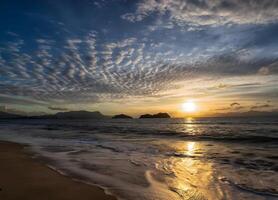 le coucher du soleil plus de le océan avec des nuages et montagnes dans le Contexte photo