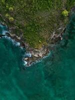 aérien. foncé turquoise l'eau avec blanc mousseux vagues et vert rocheux rive photo