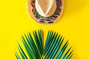 chapeau de paille et lunettes de soleil avec des feuilles de palmier vertes sur fond jaune vif. concept d'été, voyage à la plage. photo