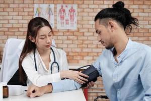 belle femme médecin en chemise blanche qui est une personne asiatique avec stéthoscope examine la santé d'un patient masculin dans une clinique médicale de fond de mur de briques, conseillant une profession de spécialiste médical. photo