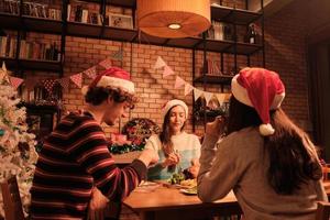 les amis s'amusent à dîner à table avec des aliments spéciaux, tels que la dinde rôtie et le vin dans la salle à manger de la maison, décorée d'ornements, le festival de Noël et la fête du nouvel an. photo