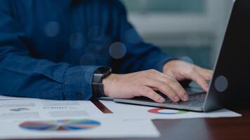 une homme d'affaire est dactylographie sur une portable tandis que à la recherche à une bouquet de papiers. le papiers sont propager en dehors sur le tableau, et le directeur est concentré sur le sien travail. concept de productivité et concentration photo