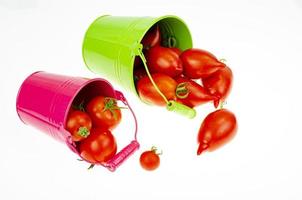 récolte. tomates mûres rouges dans des seaux colorés sur fond blanc. photo d'atelier.