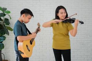 asiatique garçon en jouant guitare et mère en jouant violon, ressentir apprécié et encouragé. concept de une content famille, apprentissage et amusement mode de vie, l'amour famille cravates photo