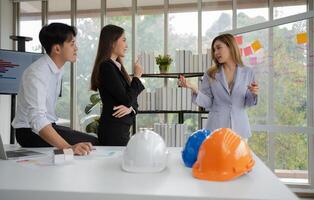 groupe de asiatique hommes d'affaires et ingénieurs travail et réflexion dans bureau. compétent construction équipe ayant discussion pendant réunion. équipe architecte à la recherche à plans dans une bâtiment site photo