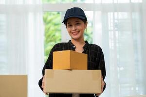 souriant Jeune femme en portant papier carton boîte, en ligne achats livraison concept. en ligne commercialisation et livraison. Jeune asiatique fille en portant et porter marron des boites pour livraison à le client. photo