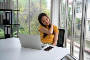 magnifique Jeune asiatique femme d'affaires, épaules et retour douleur pendant travail longue temps sur lieu de travail. corps muscles rigide problème après longue journée travail et surmené. Bureau syndrome et soins de santé concept. photo