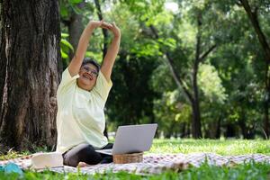 content asiatique Sénior femme en utilisant portable pour travail en ligne à l'extérieur bureau. personnes âgées retraite en utilisant portable pour apprentissage Nouveau compétence et free-lance travail dans parc, Sénior mode de vie avec La technologie photo