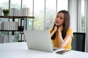 magnifique Jeune asiatique femme d'affaires, épaules et retour douleur pendant travail longue temps sur lieu de travail. corps muscles rigide problème après longue journée travail et surmené. Bureau syndrome et soins de santé concept. photo