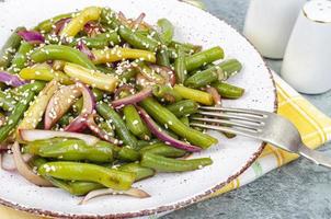 plat végétarien de gousses de haricots verts avec oignons rouges marinés et graines de sésame. studio photo