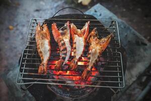 grand crevettes sont mis sur un le fer plaque et grillé plus de une chaud charbon poêle. photo