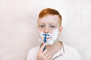 peu garçon est rasage le sien visage dans le salle de bains photo