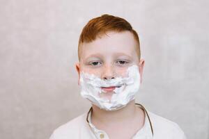 marrant garçon dans le une baignoire avec rasage crème sur le sien visage photo