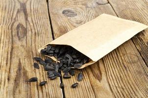 graines de tournesol noires non pelées dans un sac artisanal sur une table en bois. photo