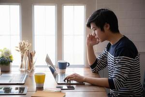 asiatique homme étudiant concentrer apprentissage en ligne cours et en train de regarder Didacticiel via portable ordinateur à vivant pièce dans maison,. en ligne classe pièce concept. photo