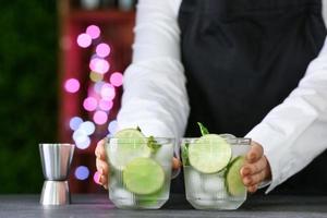 barman féminin avec des verres de mojito frais sur table en bar photo