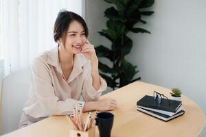 portrait de content femme séance à sa bureau. attrayant Jeune sur de soi affaires femme ou comptable souriant et avoir idée pour sa gros projet. photo