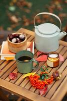 une tasse de thé ou café et une livre sur une en bois table contre le Contexte de déchue feuilles, l'automne saison, encore la vie avec feuilles, une livre et viorne et châtaignes dans le jardin en plein air. photo