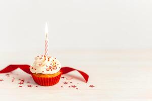 anniversaire petit gâteau avec crème au beurre glaçage, rouge ruban et bougie sur blanc en bois tableau. photo