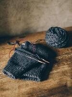 main tricoté chaussette avec aiguilles et gris fil Balle sur foncé en bois Contexte. photo