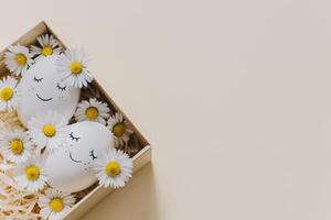 mignonne des œufs avec Marguerite fleurs dans une boîte sur une Jaune pastel Contexte. Pâques Contexte. photo